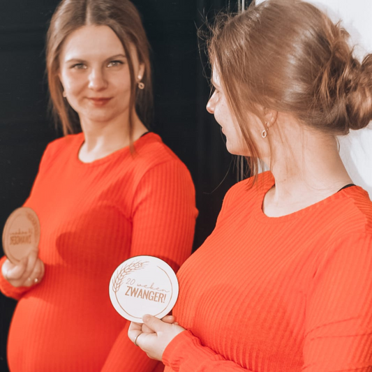 Mijlpaalkaart 20 weken zwanger in de hand van een zwangere vrouw voor een spiegel.