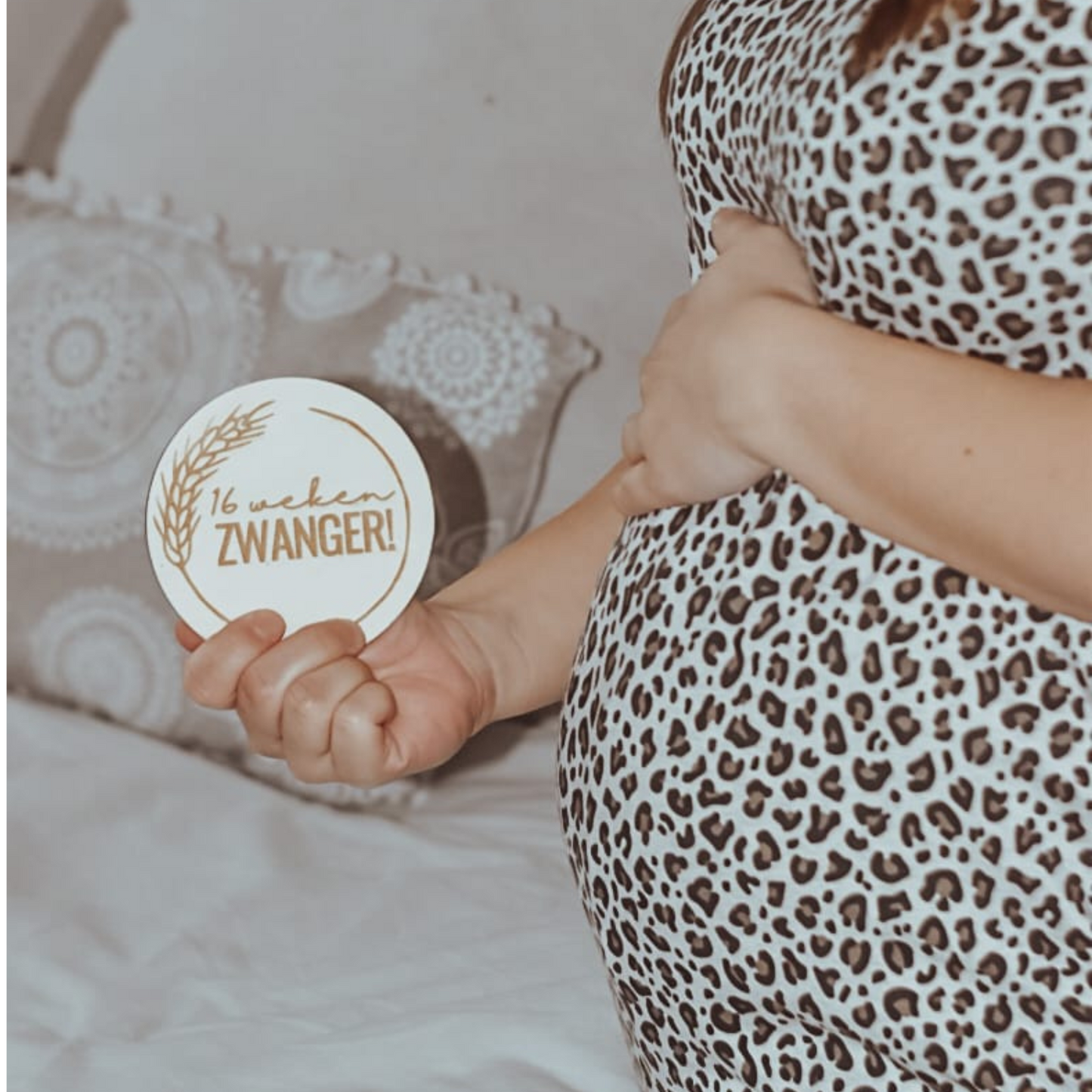 Zwangere vrouw houdt een mijlpaalkaart met 16 weken zwanger bij haar buik.